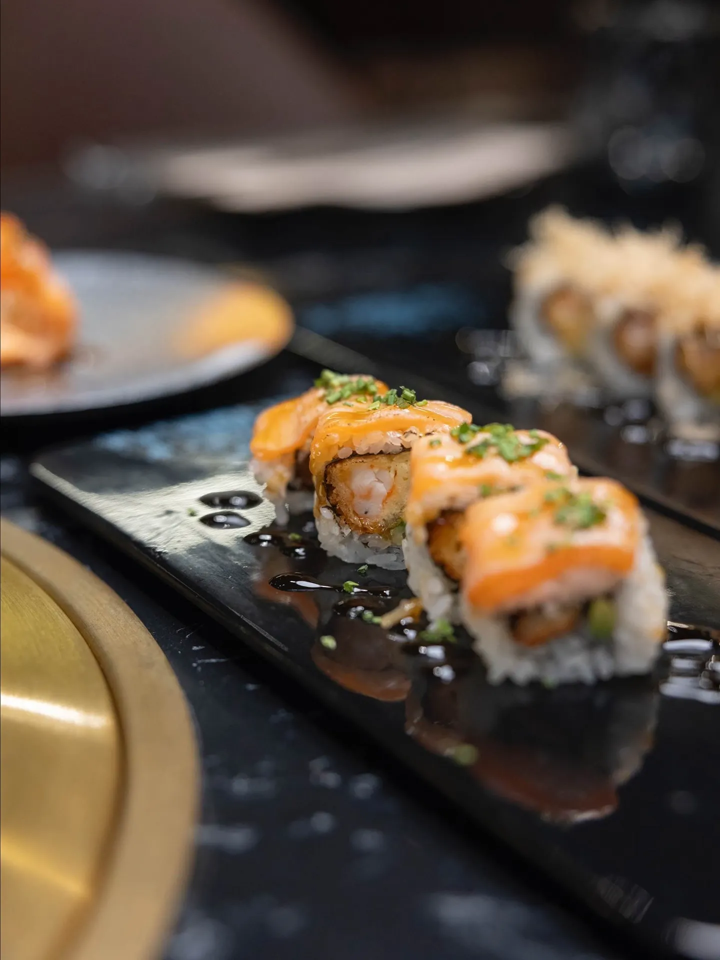 Sushi de salmón servido en un plato negro, con salsa y decorado con cebollín, en un ambiente elegante de restaurante japonés.