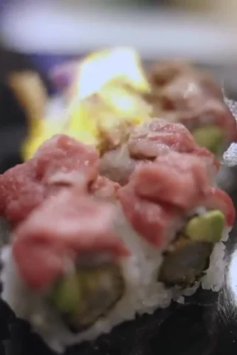 Sushi gourmet con capas de pescado fresco y vegetales, presentado en un plato elegante. Ideal para amantes de la cocina japonesa.